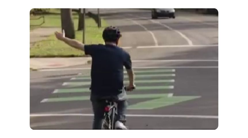 A man signaling a left hand turn on his bike