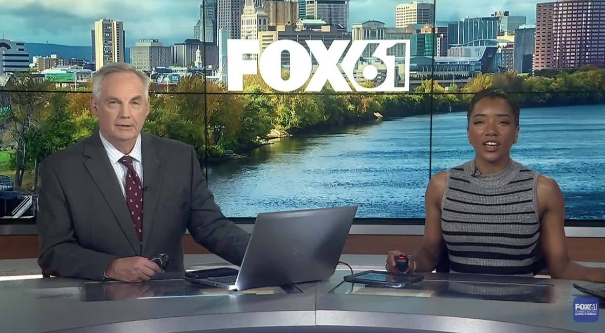 Two news broadcasters sitting in a FOX 61 newsroom making an announcement.